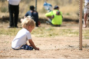 A child plays in the dirt waiting for Dad to finish the race. 