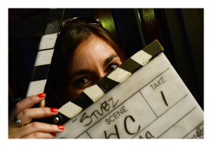 Romina, an actress in a tv pilot being filmed in the room behind her, holds the slate used to set up the shot.